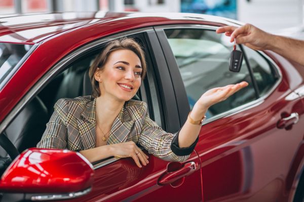Woman sitting inside a red car receiving keys from another person